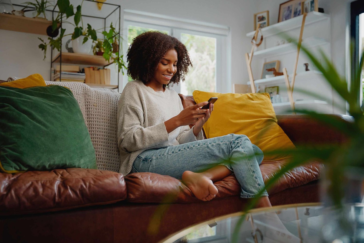 Image shows young woman sitting on a sofa looking at a phone screen