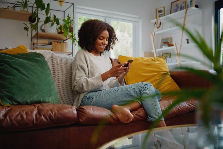 Image shows young woman sitting on a sofa looking at a phone screen