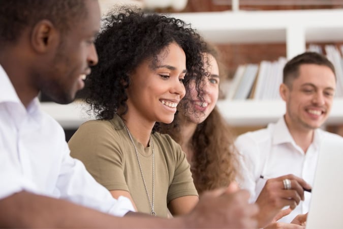 Image shows group of smiling people looking at a laptop