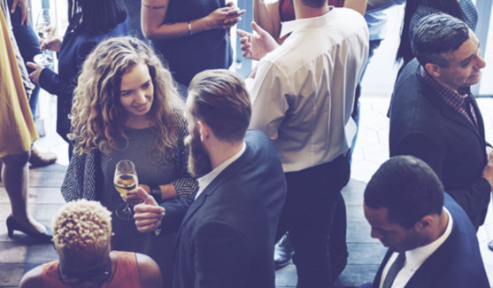 Image shows a gathering of people from above holding wine glasses