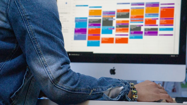 Image shows a desktop monitor with a kanban board on screen with someone's arm in view
