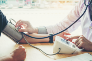 Image shows someone holding a stethoscope against an arm in a pressure cuff